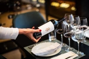 PerUs wine being poured into empty wine glasses at a table set for a meal