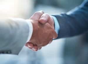 Two men in gray suit and navy suit shake hands in agreement. 